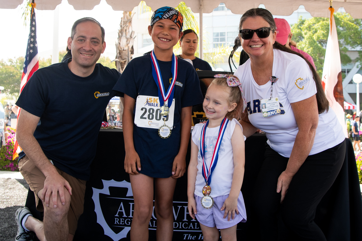 Arrowhead Regional Medical Center (ARMC) Chief Executive Officer, Andrew Goldfrach, FACHE, and ARMC Chief Nursing Officer, Sharon Brown, celebrate with two young walkers on stage at the May 2, 2026, ARMC 5K Walk/Run in Colton.